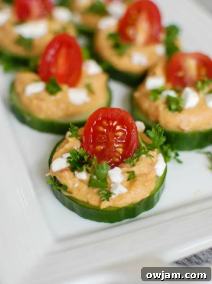 Cucumber Hummus Bites make the perfect finger food and appetizer for your next party or get together. Crisp cucumbers slices are topped with roasted red pepper hummus, tomatoes, feta cheese and fresh parsley. 