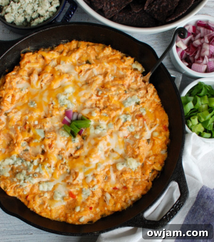 Bubbling hot Buffalo Queso Cheese Chicken Dip in a rustic skillet, garnished with blue cheese and green onions, ready for game day