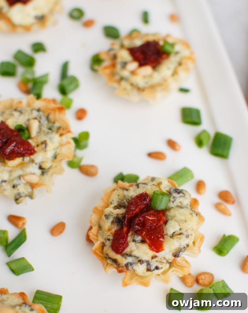 Crispy spinach artichoke sun-dried tomato phyllo bites appetizer on a white plate, perfect for holiday gatherings