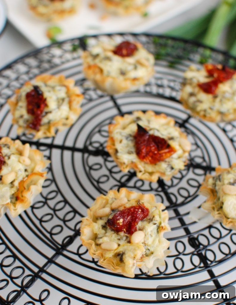 Freshly baked spinach artichoke sun-dried tomato phyllo bites cooling on a wire rack