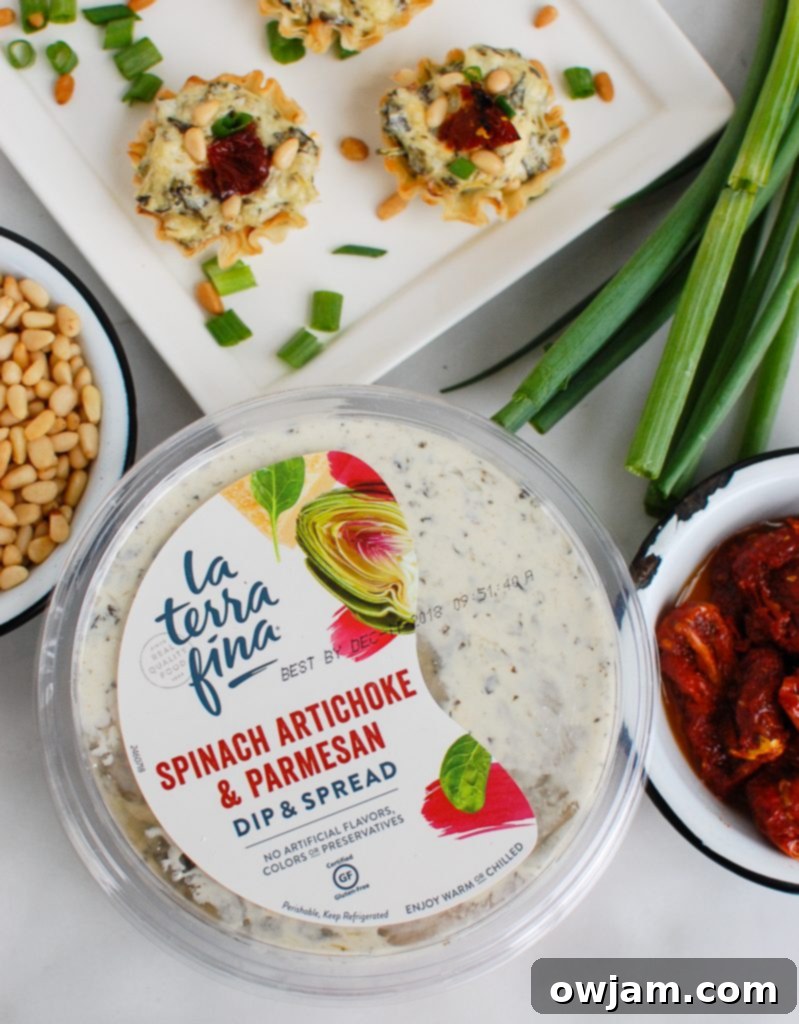 Close-up of spinach artichoke sun-dried tomato phyllo bites next to a tub of La Terra Fina Spinach Artichoke & Parmesan Dip