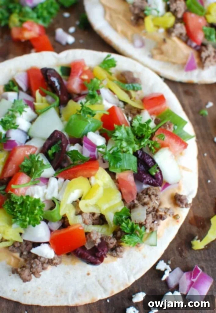 Close-up of a delicious Greek Beef Pita Pizza, showcasing fresh toppings and seasoned ground beef.