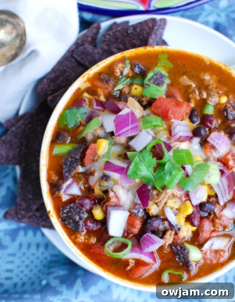 Effortless Instant Pot Turkey Chili 3 Overhead shot of Instant Pot Turkey Chili in a white bowl, ready to be served, with various toppings like cheese and cilantro in the background.