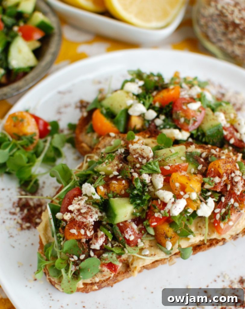 Mediterranean Hummus Toast with Za'atar on White Plate - A delicious Mediterranean hummus toast topped with fresh tomatoes, cucumbers, herbs, and feta, sprinkled with za'atar.