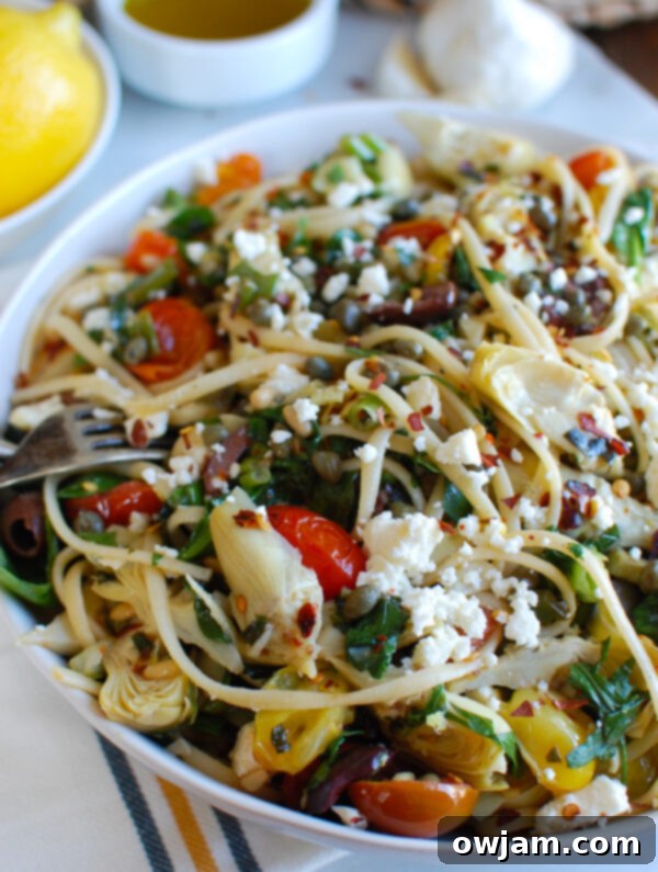 Sun-Kissed Mediterranean Pasta 5 Close-up of Mediterranean Pasta in a white bowl, generously garnished with fresh feta cheese, chopped parsley, and basil.