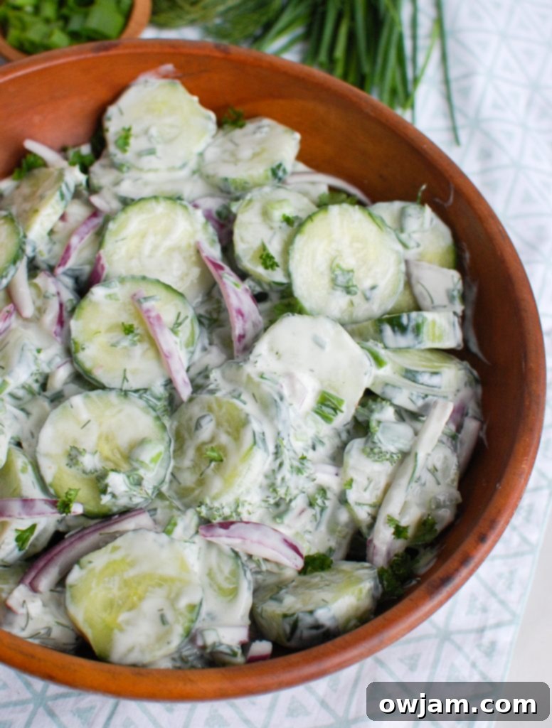 Large wooden bowl filled with creamy cucumber salad, garnished with fresh dill