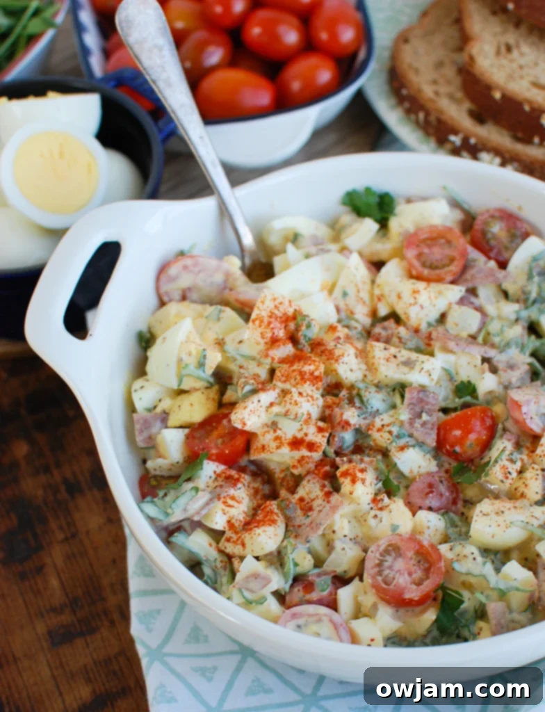 Creamy Bacon Egg Salad in a white bowl, garnished with fresh herbs.