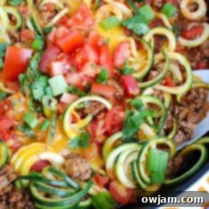 Mexican Zucchini in skillet, generously topped with melted cheese, diced tomatoes, cilantro, and green onions, ready for serving.
