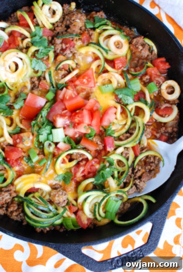 A vibrant serving of Mexican Zucchini in a white bowl with a spoon, highlighting the delicious texture and fresh, colorful toppings of the low-carb dish.