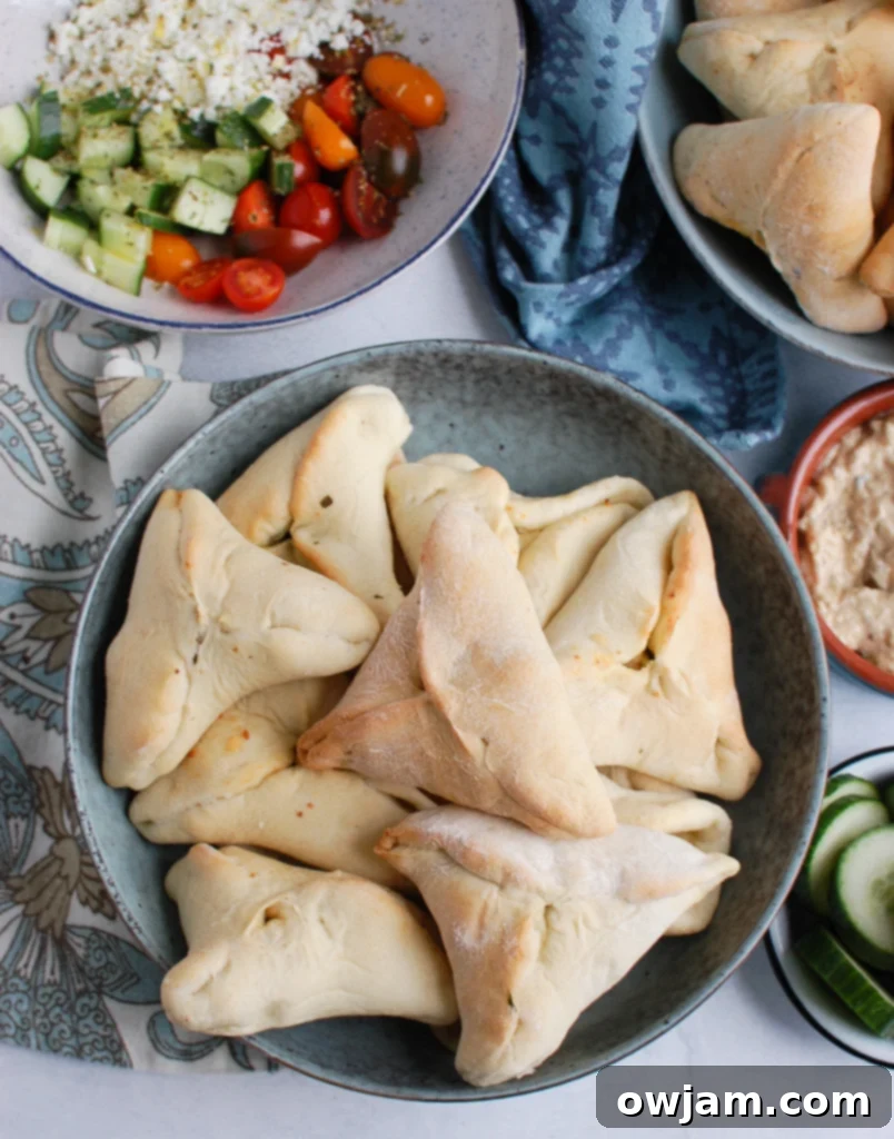 A large rustic bowl filled with numerous freshly baked, golden spinach fatayer triangles, ready for a gathering.