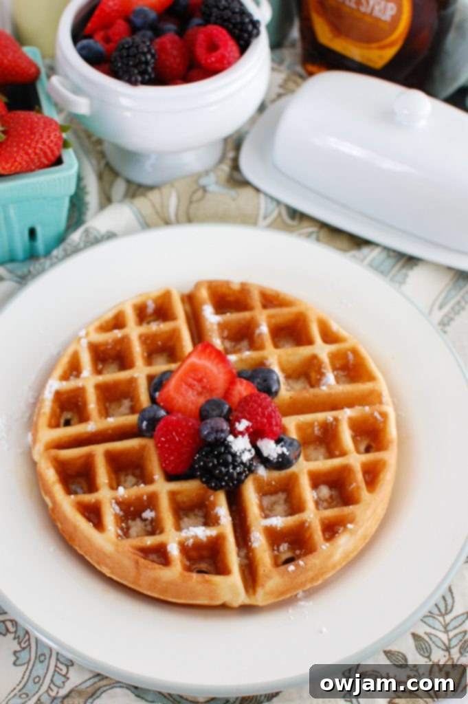 A beautiful stack of Greek Yogurt Waffles, lightly dusted with powdered sugar and adorned with a colorful array of fresh berries, emphasizing their delicious appeal.