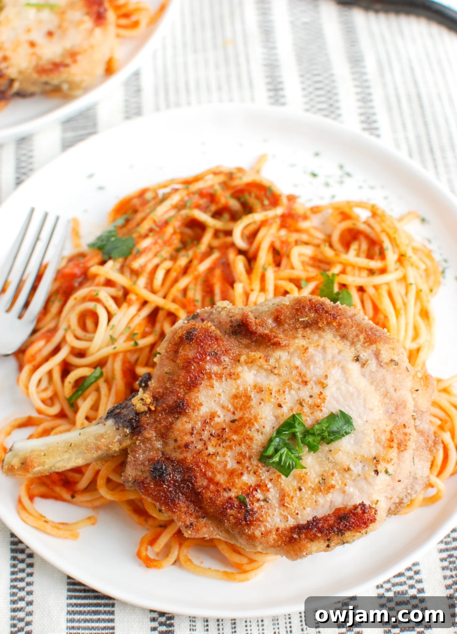 Perfect Oven-Baked Pork Chops 4 Plated oven-baked breaded pork chops served alongside fresh pasta and a rich tomato sauce, garnished with parsley.
