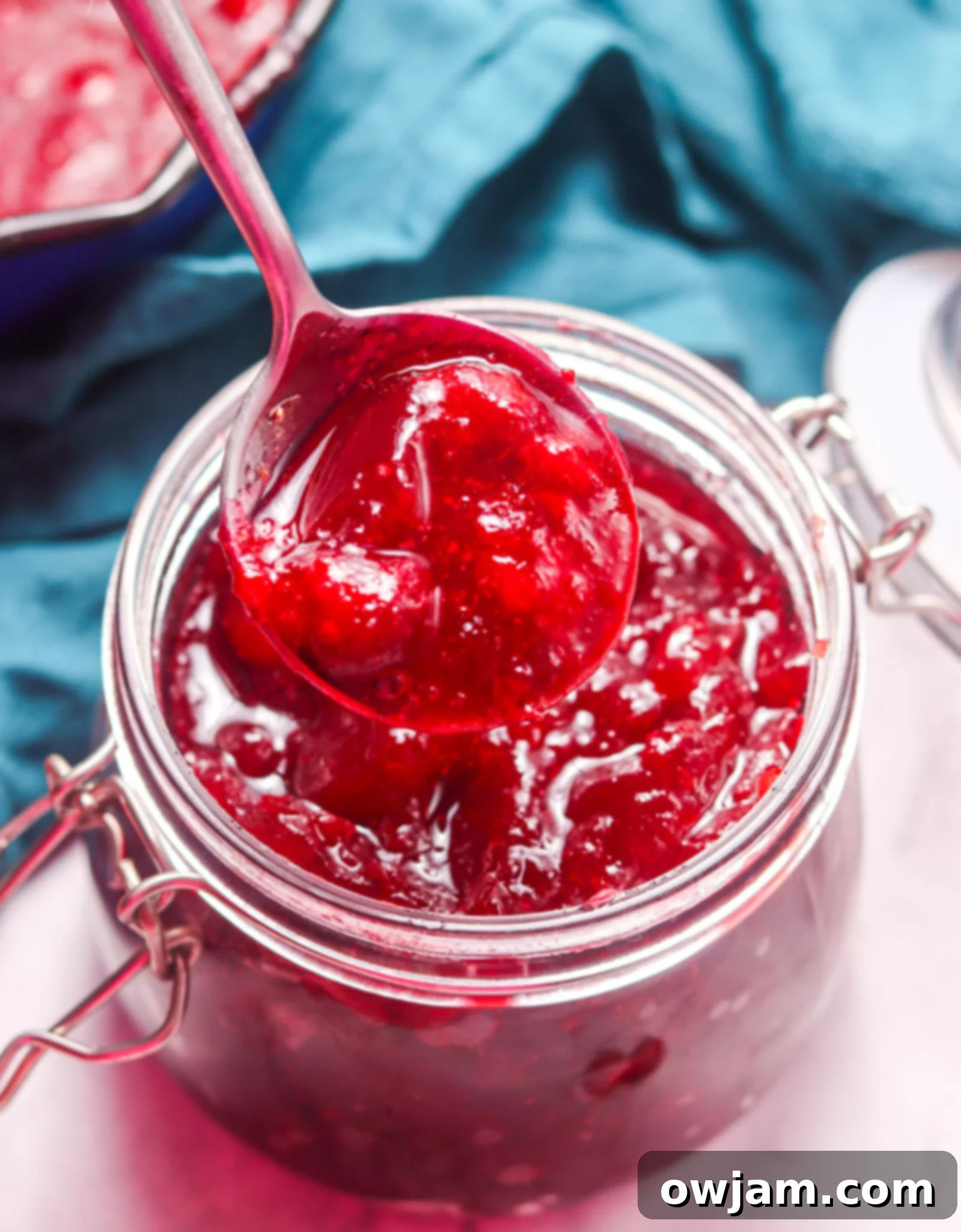 Homemade Cranberry Sauce Recipe in a glass jar with a spoon, showing its vibrant color and texture.