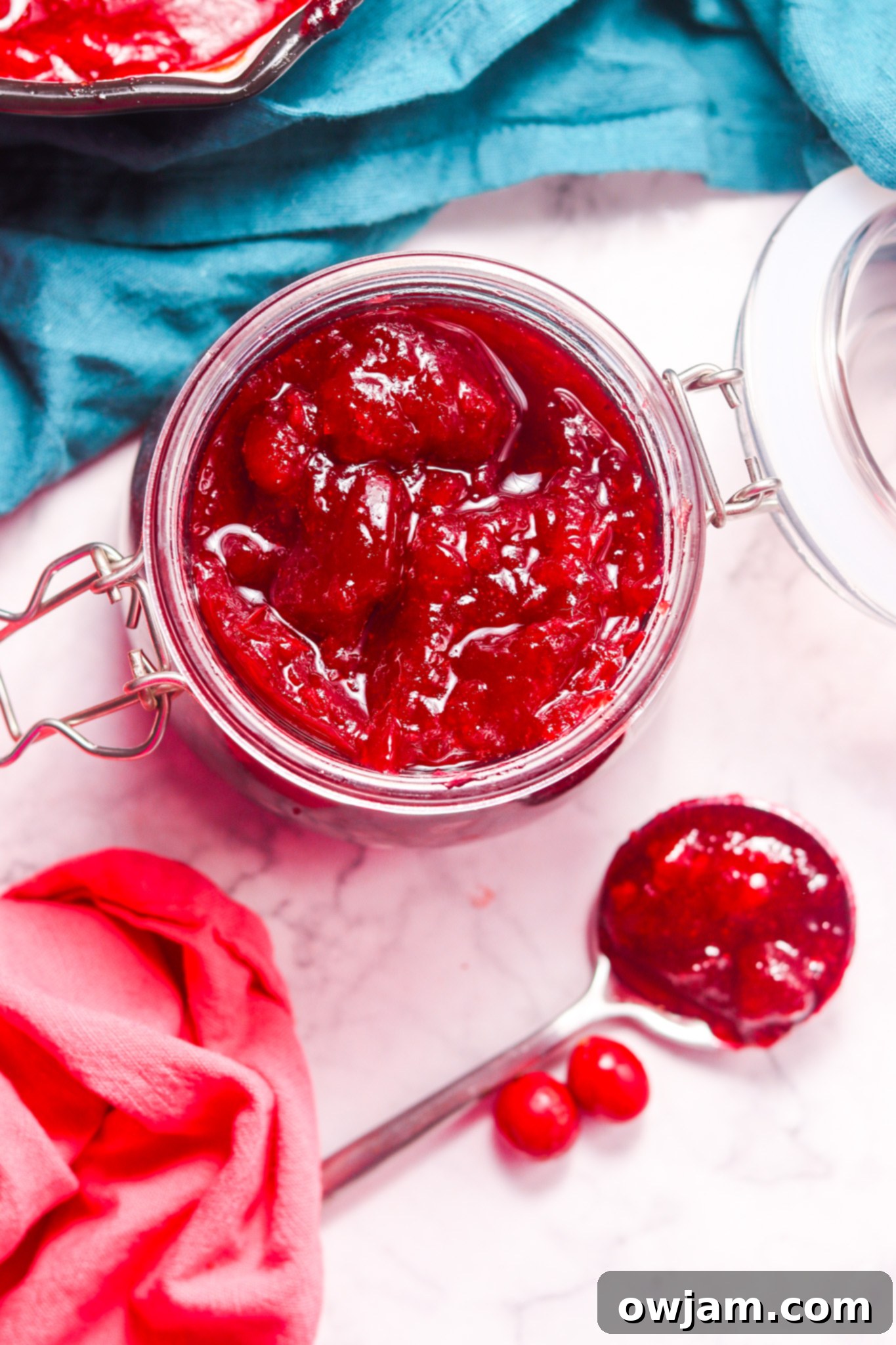 Homemade Cranberry Sauce Recipe in a glass jar with a spoon resting on the rim, set against a rustic background.