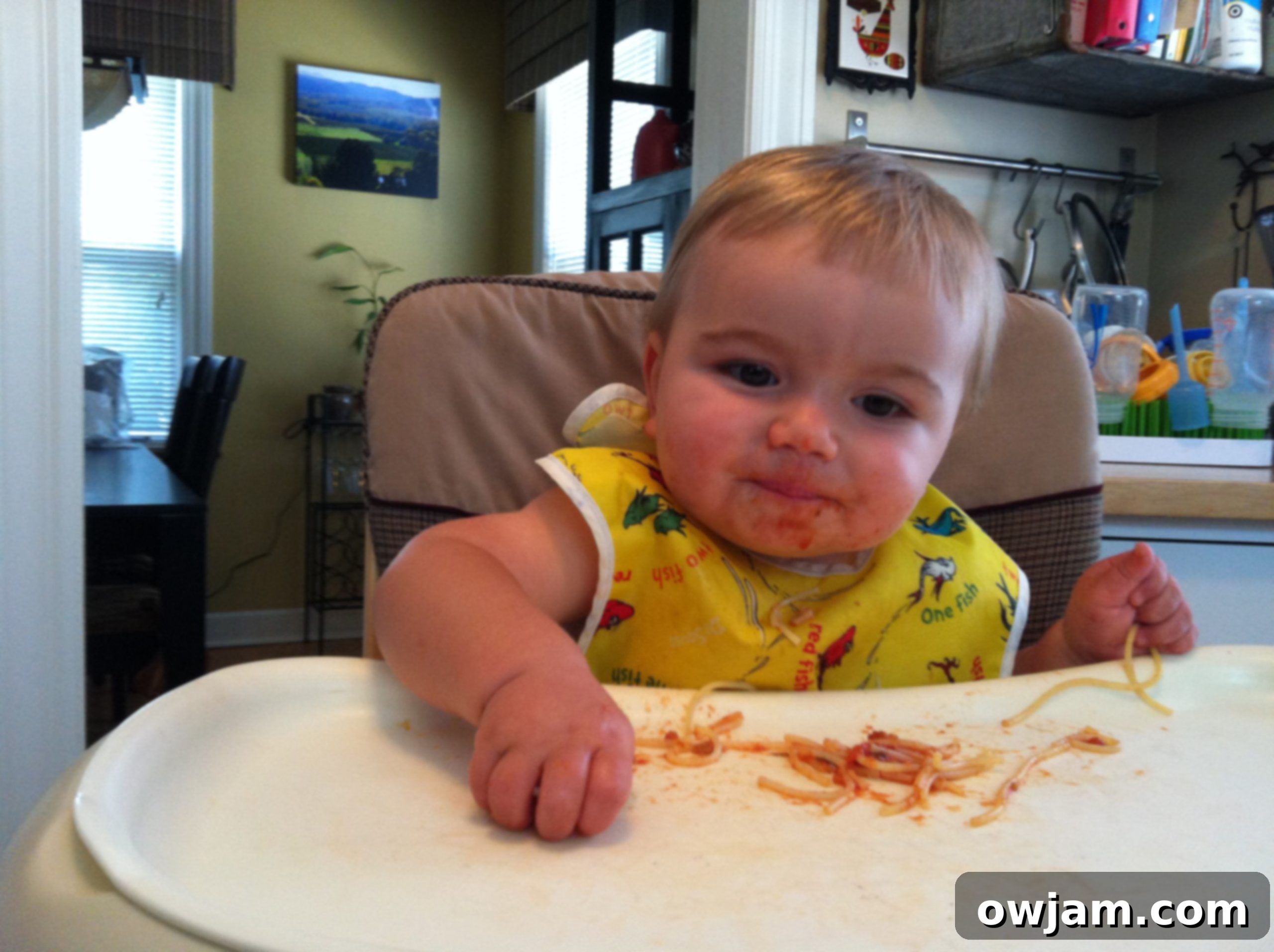 Happy baby eating spaghetti for the first time, with a playful, messy expression
