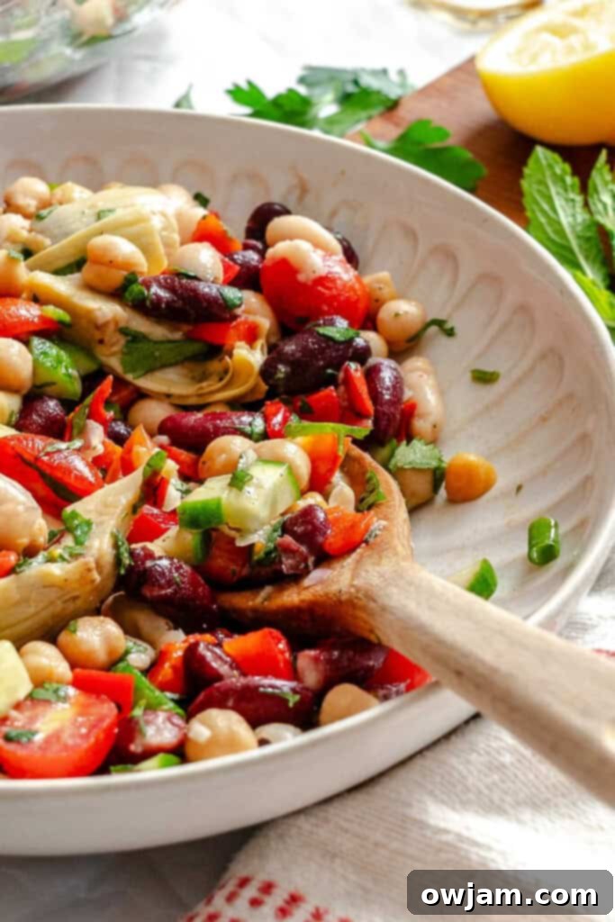 A vibrant Mediterranean Three Bean Salad served in a white bowl, garnished with fresh herbs, showcasing its rich colors and textures.