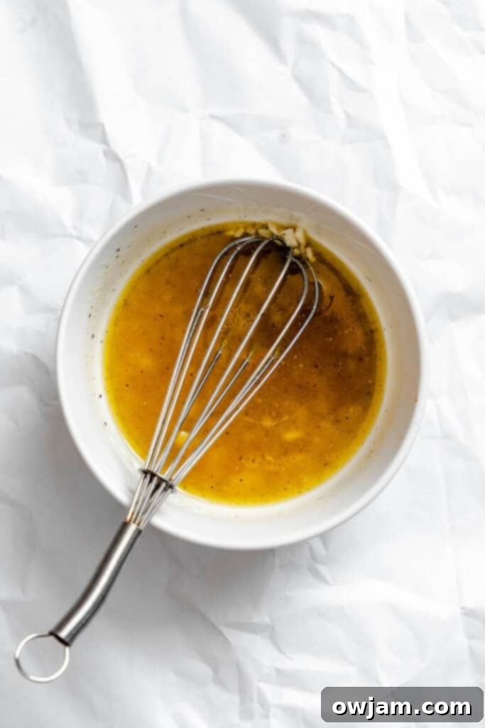 Ingredients for the salad dressing in a bowl, with a whisk, ready to be mixed. Includes olive oil, lemon, and spices.