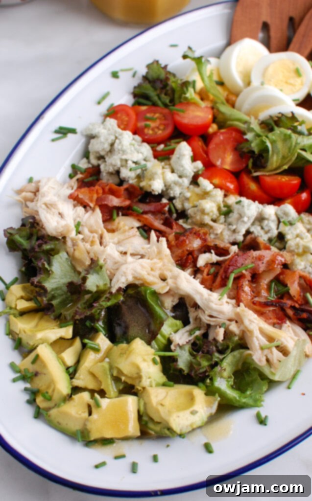 The Ultimate Cobb Salad 4 Close-up of Cobb Salad being served with wooden tongs, highlighting the layers and freshness of ingredients.