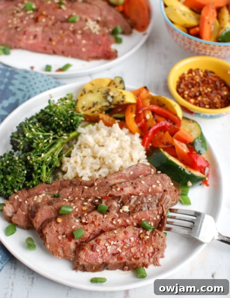 Close-up of a perfectly cooked and sliced Asian Marinated Flank Steak on a white plate, garnished with herbs
