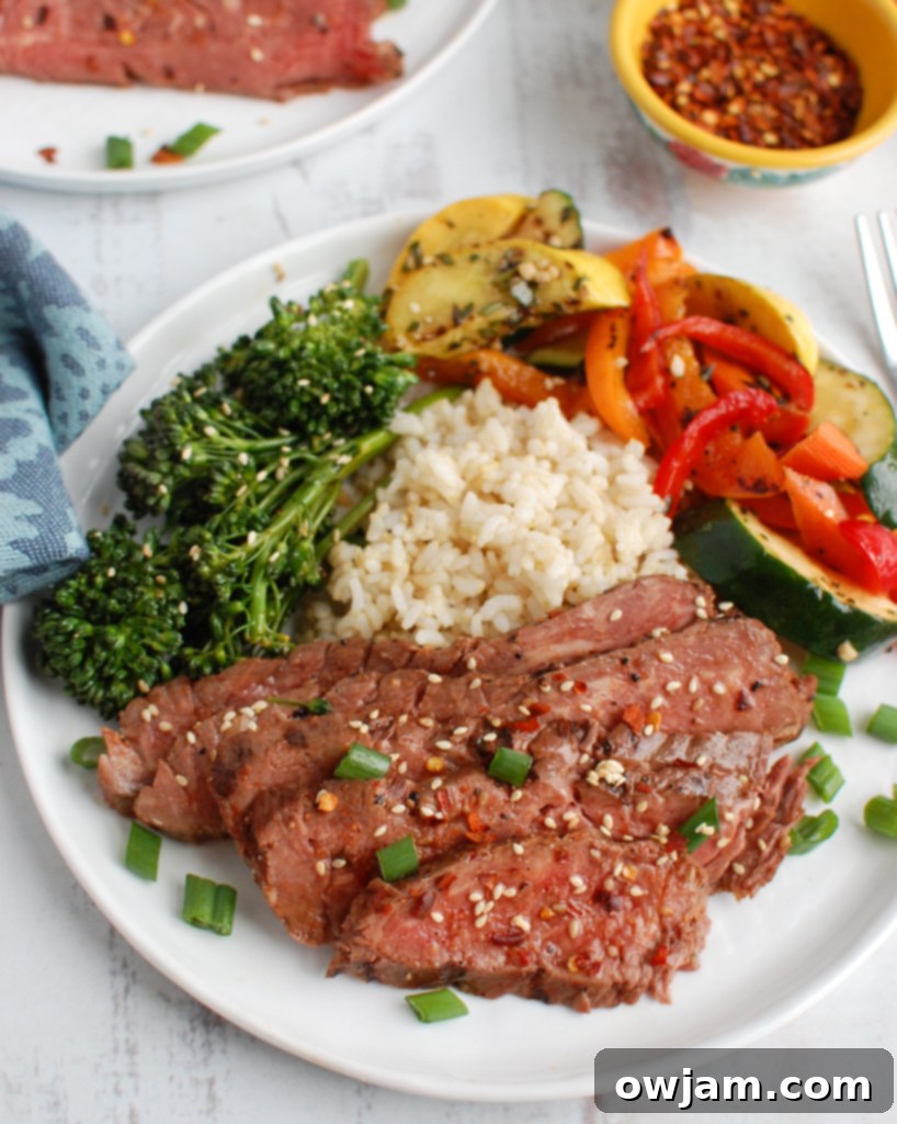 A fork piercing a tender slice of Asian Marinated Flank Steak, showing its succulent texture