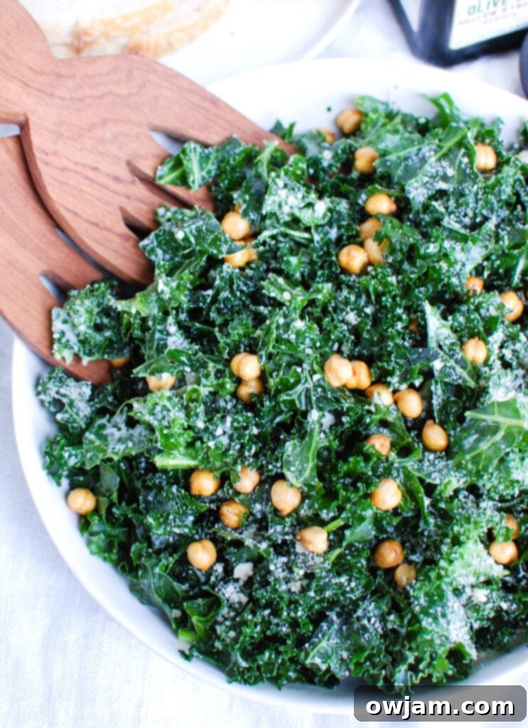 Elevated Kale Caesar 3 Kale Caesar Salad being tossed with wooden tongs in a large white bowl, showing tender kale and crispy chickpeas.