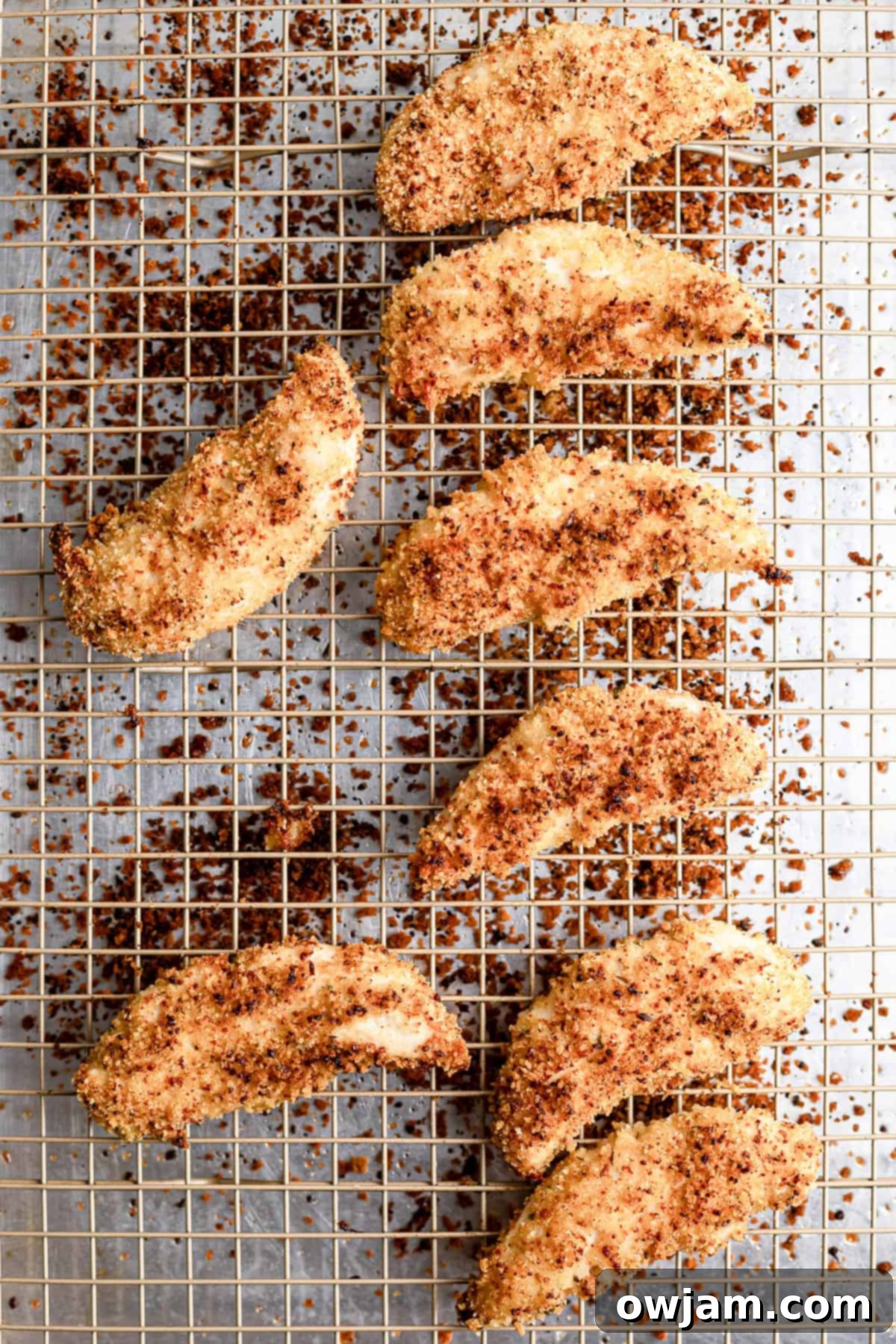 Super Crispy Easy Baked Chicken Tenders 7 Cooked baked chicken tenders cooling on a wire rack, showcasing their golden and crispy exterior.