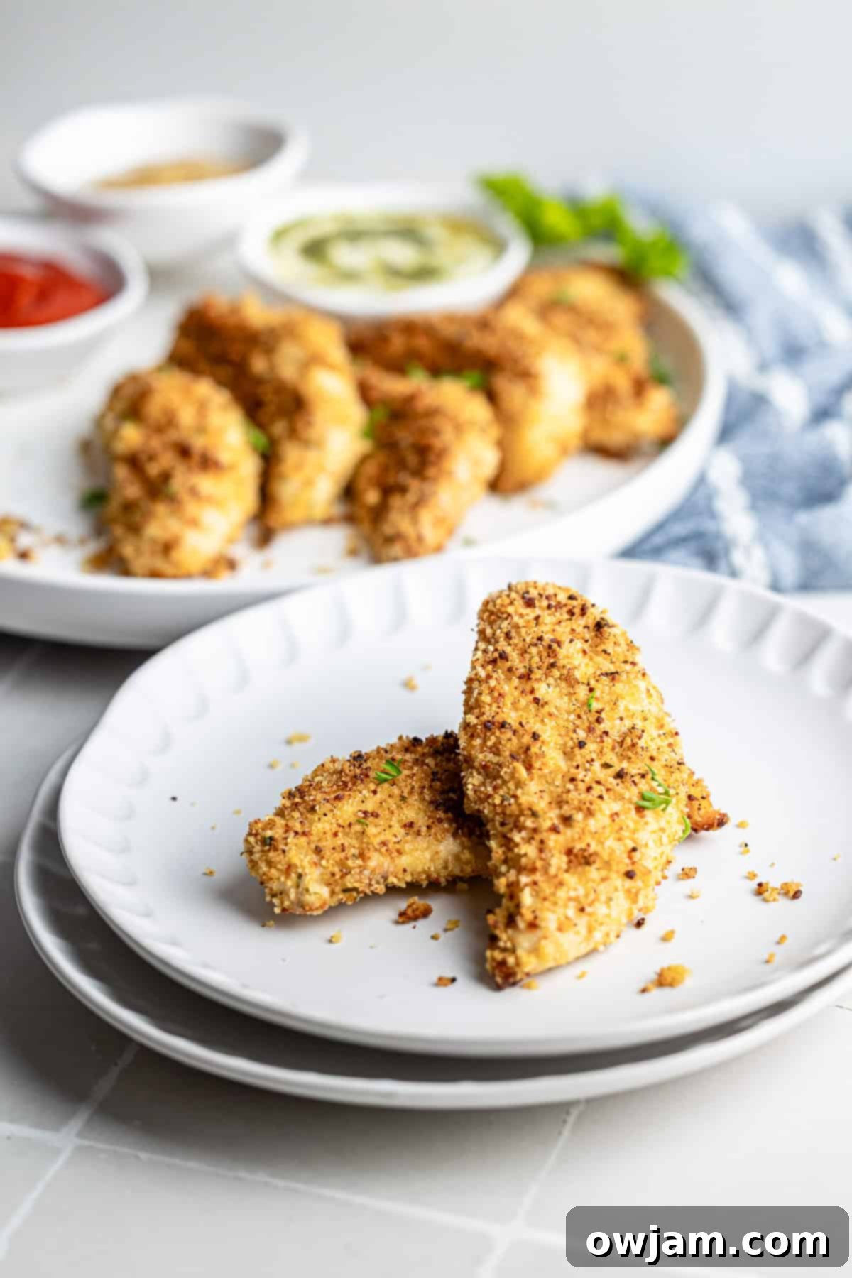 Super Crispy Easy Baked Chicken Tenders 8 Baked chicken tenders plated on a white dish with fresh herbs for garnish, ready to be served.