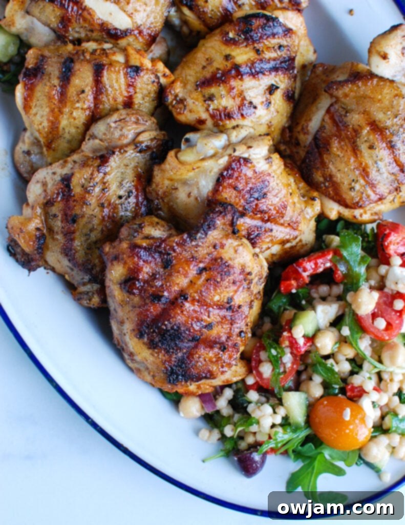 Grilled Greek Chicken Thighs on platter, garnished with fresh herbs and lemon wedges