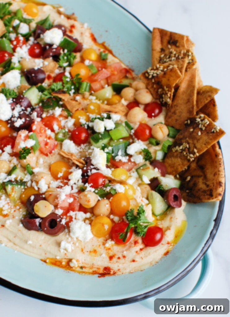 Mediterranean Hummus Mezze 2 Hummus Platter on teal plate, garnished with olives, feta, tomatoes, and herbs