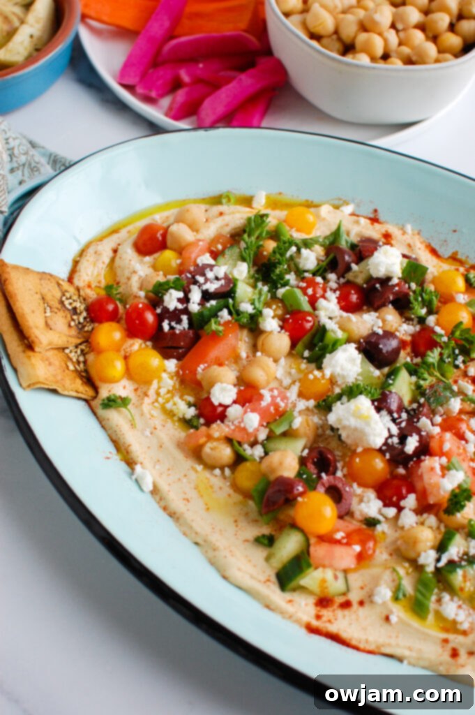 Mediterranean Hummus Mezze 4 A hummus platter served on a teal platter with a variety of pita chips and fresh vegetables around it.