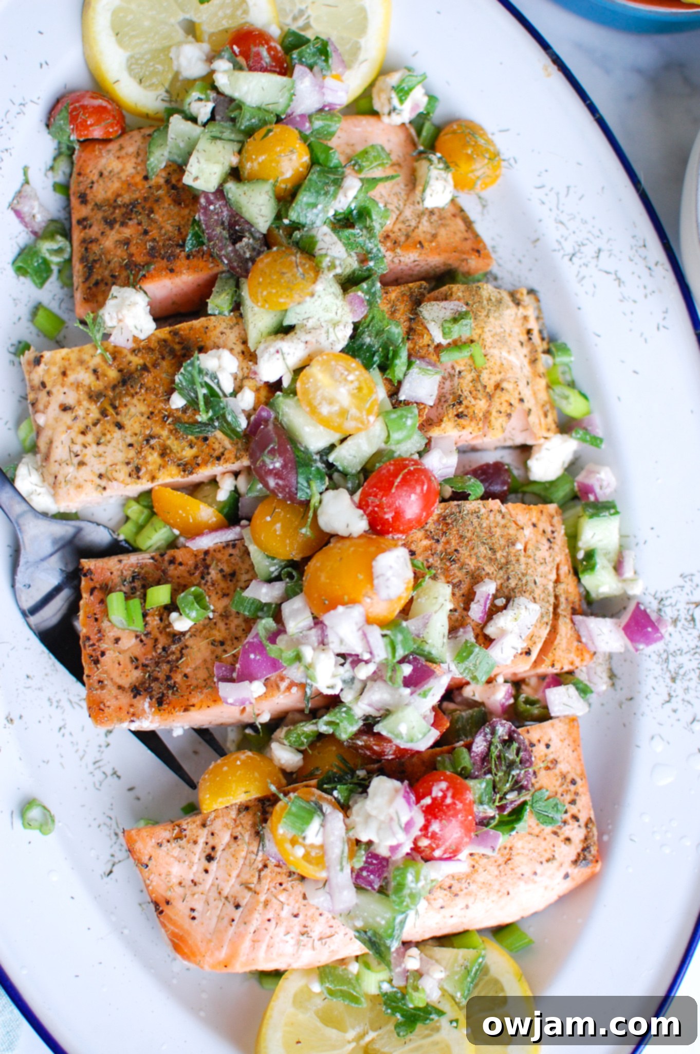 Your New Favorite Mediterranean Baked Salmon 4 Mediterranean Salmon on white platter topped with fresh tomatoes, feta cheese, and herbs.