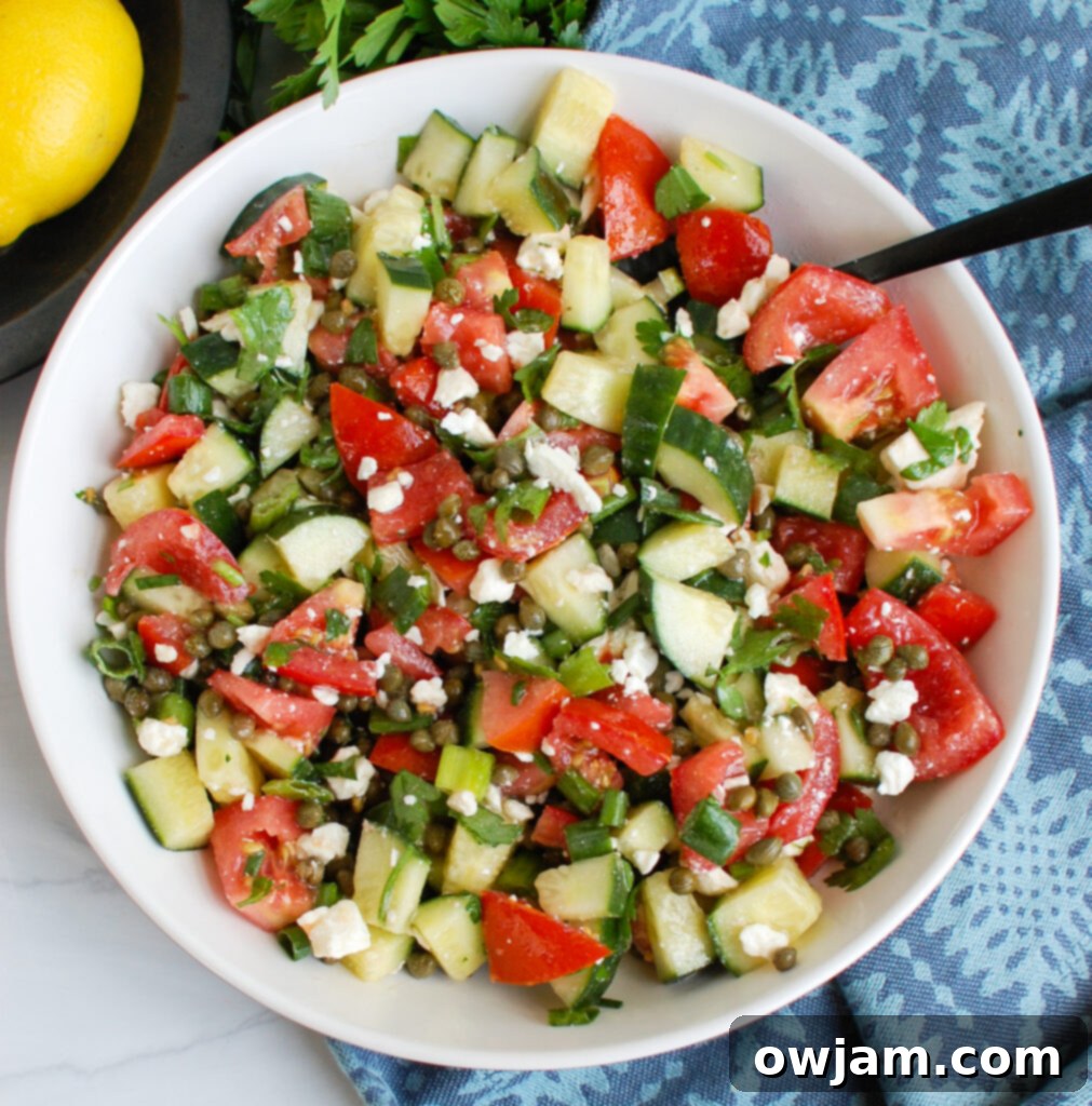 Vibrant Tomato Cucumber Caper Salad 3 Close-up of Cucumber Salad with Capers, showing creamy feta and herbs, with a spoon for serving.