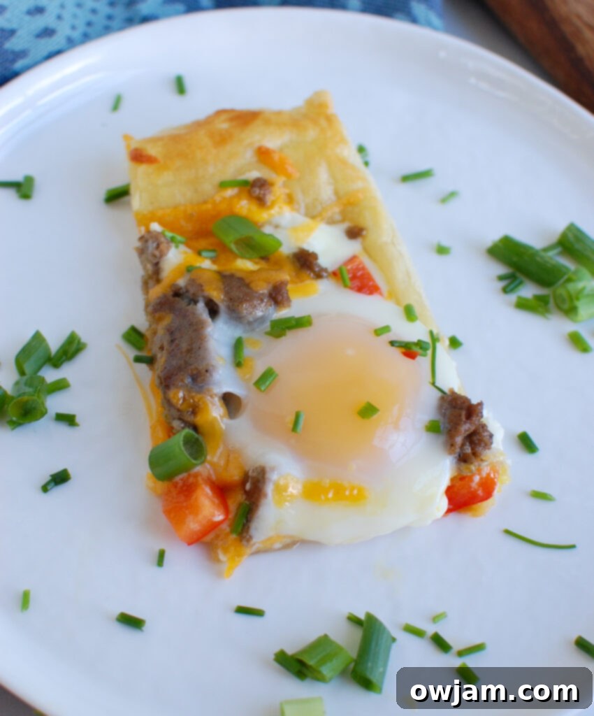 Slice of Turkey Sausage and Egg Puff Pastry Pizza on a white plate with cutlery