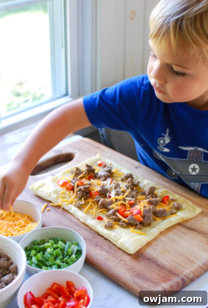 Child's hand helping to place toppings on Turkey Sausage and Egg Puff Pastry Pizza