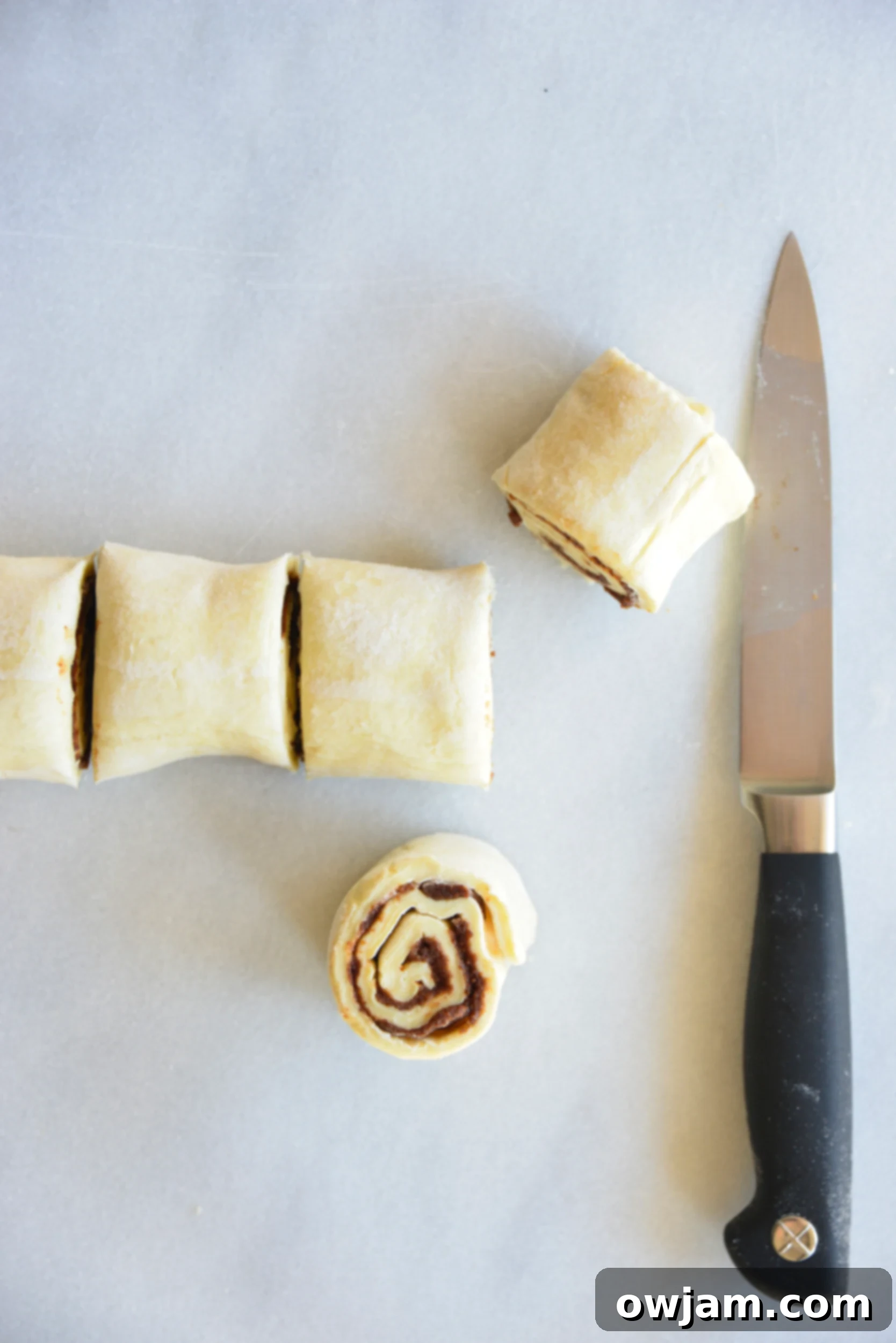 Deliciously Simple Puff Pastry Cinnamon Swirls 8 The cinnamon-filled puff pastry dough, expertly rolled into a log and placed on parchment paper, ready for slicing.