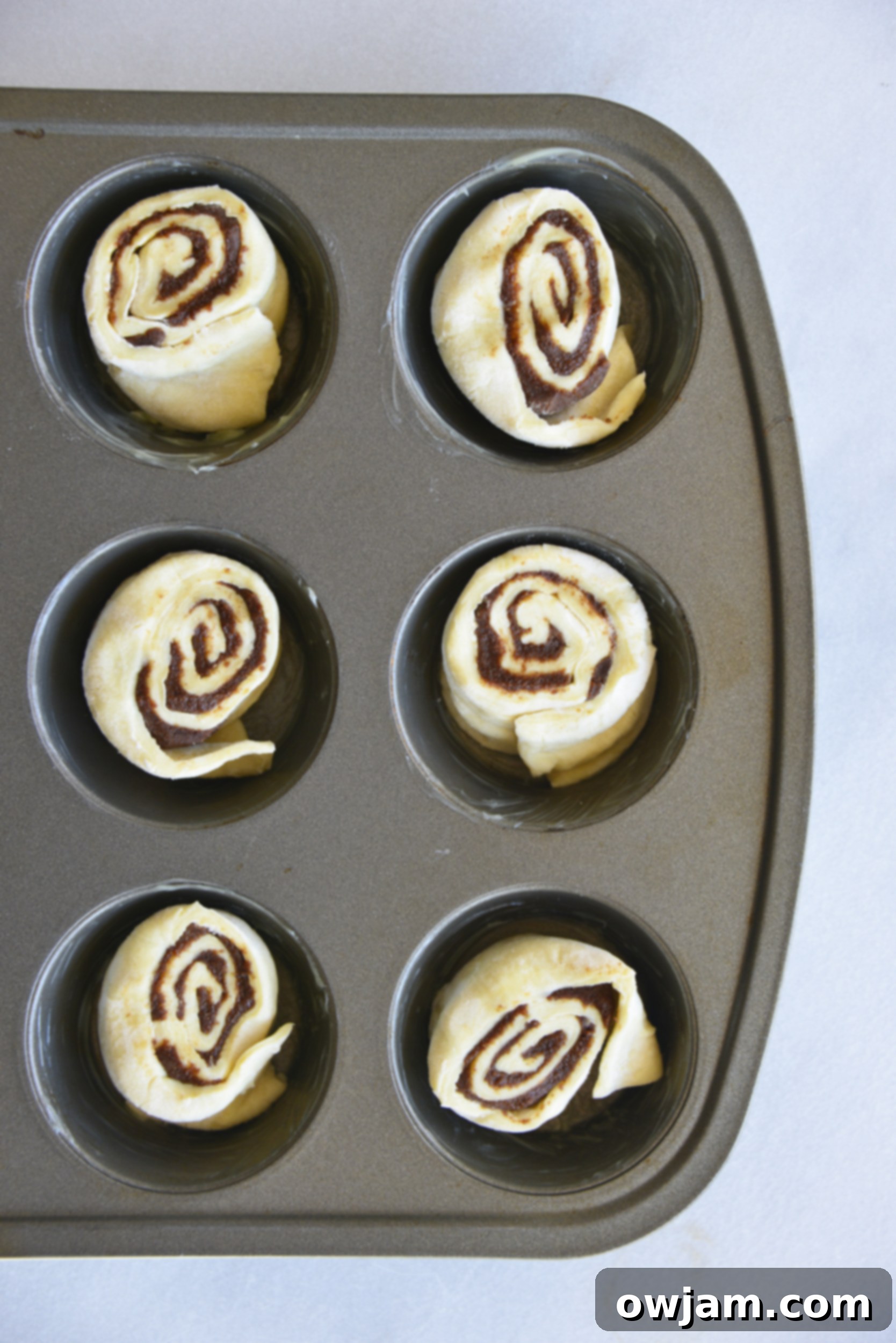 Deliciously Simple Puff Pastry Cinnamon Swirls 9 The six cut Easy Puff Pastry Cinnamon Swirls nestled into a muffin tin, prepared for baking.