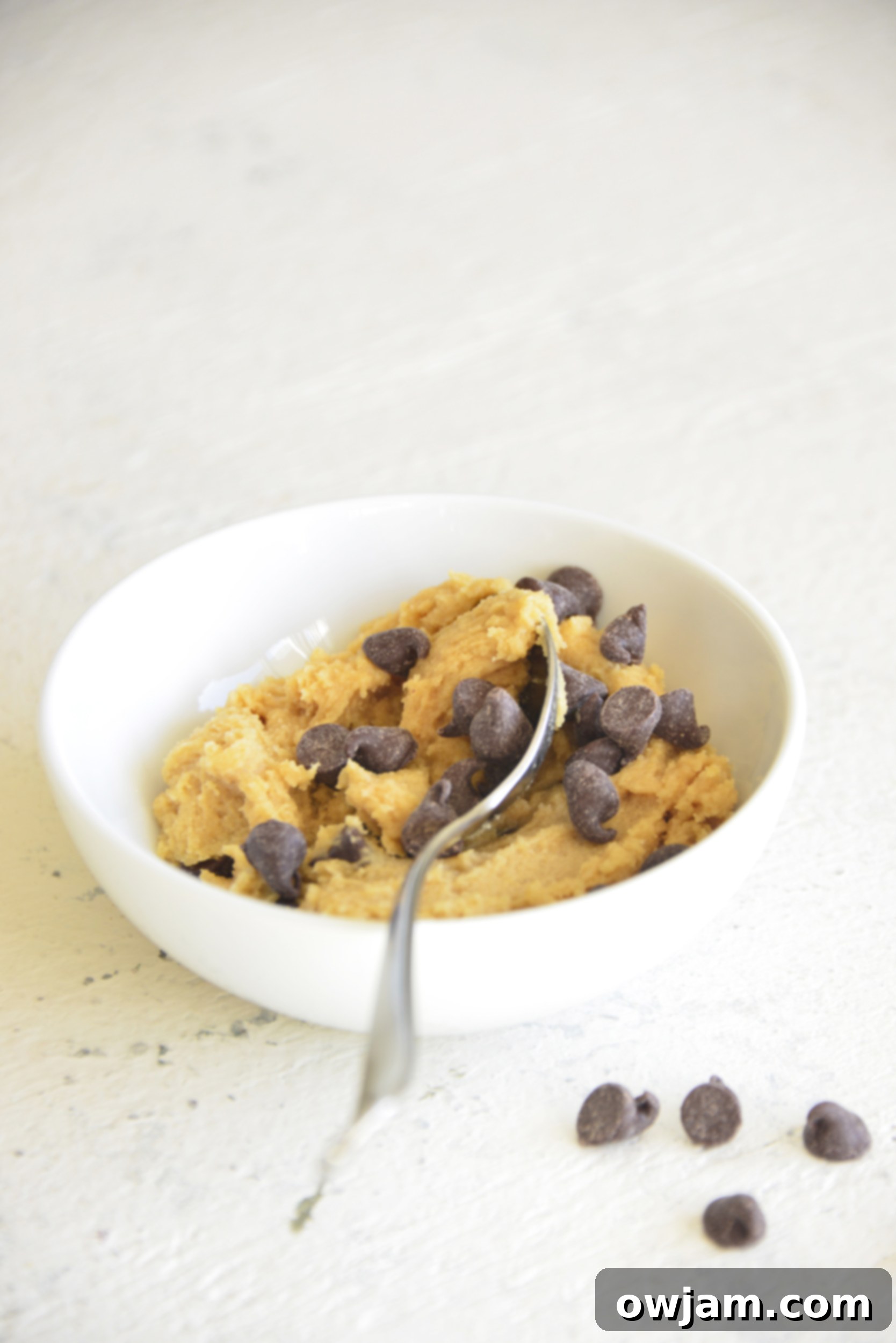 A spoon digging into a bowl of edible cookie dough for one, showcasing its tempting texture.