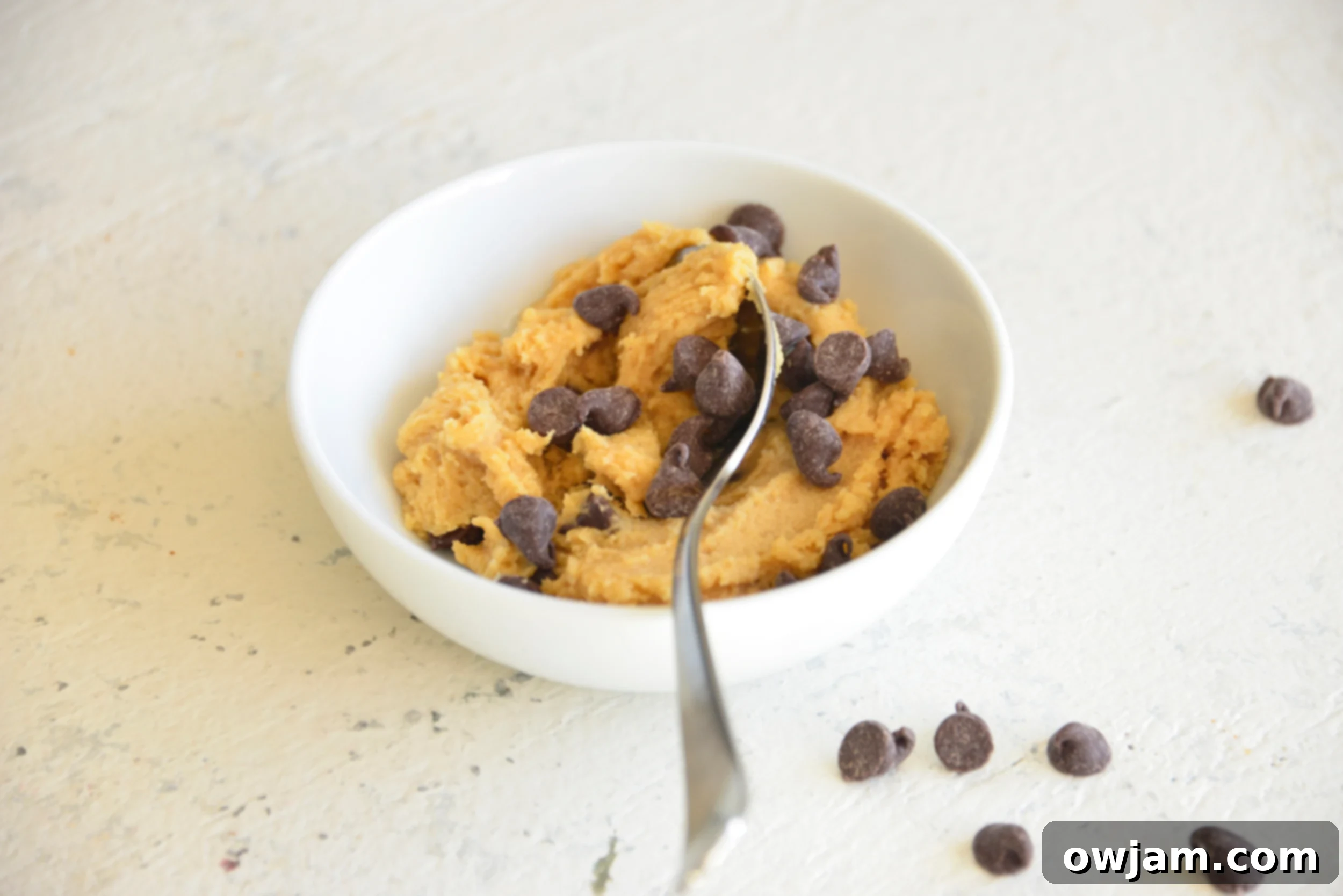 Freshly made edible cookie dough for one, with chocolate chips mixed in, in a bowl with a spoon.