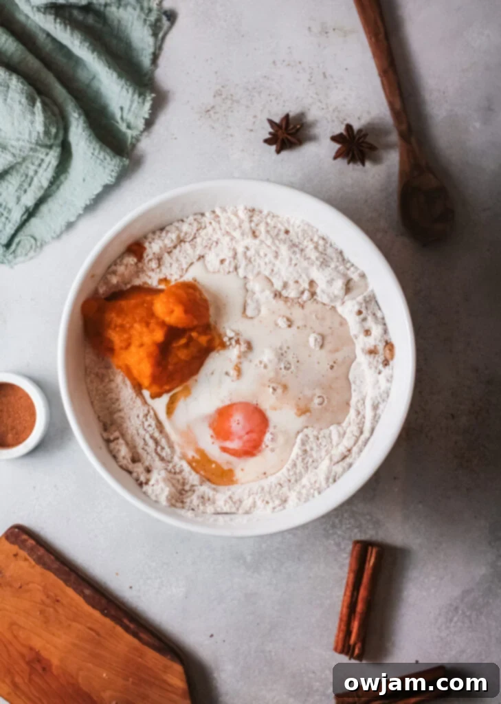 Wet ingredients, including pumpkin puree, vanilla, egg, milk, and oil, being added to the dry mixture in a bowl.