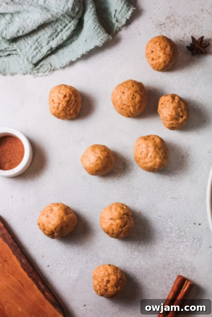 Small, uniformly-shaped pumpkin donut dough balls arranged on a parchment-lined cookie sheet.