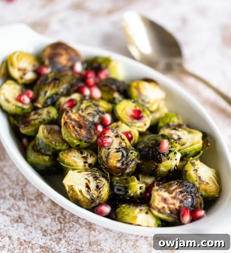 Caramelized Balsamic Brussels Sprouts 2 Delicious Roasted Balsamic Brussels Sprouts in a white serving dish, garnished with fresh pomegranate arils.