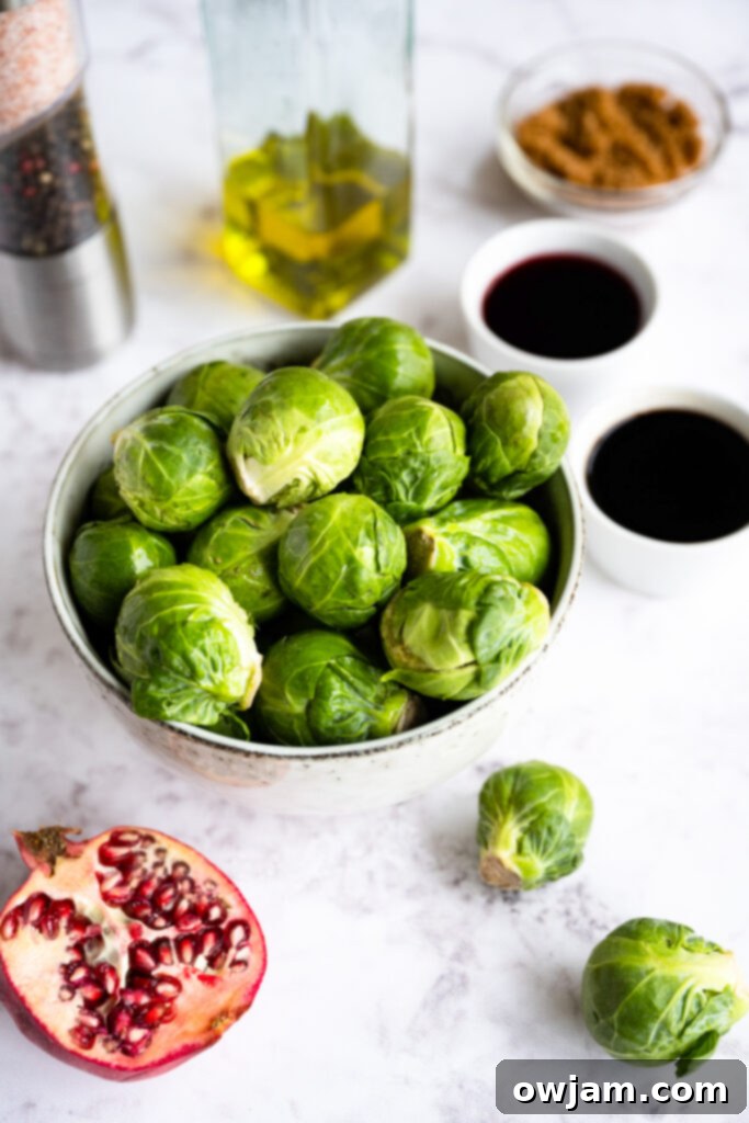 Caramelized Balsamic Brussels Sprouts 3 Ingredients for Roasted Balsamic Brussels Sprouts laid out on a wooden surface, including fresh Brussels sprouts, olive oil, balsamic vinegar, pomegranate juice, brown sugar, and pomegranate arils.