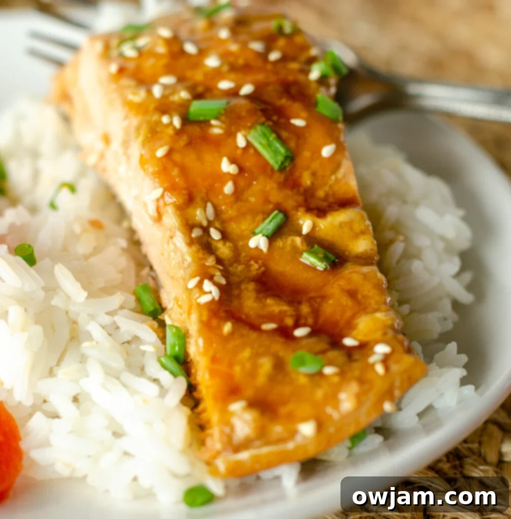 Perfectly cooked Teriyaki Salmon on a white plate, garnished with sesame seeds and chives, ready to be served