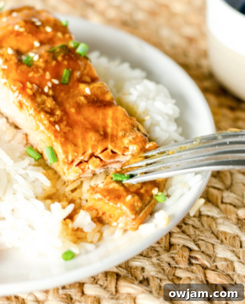 A fork taking a piece of flaky Teriyaki Salmon from a white plate