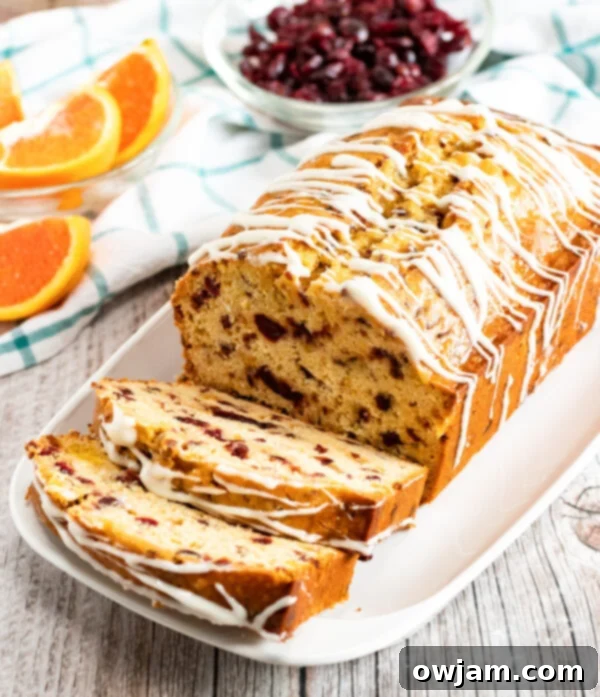 Cranberry Orange Bread Recipe loaf on a white plate with orange slices, topped with white icing