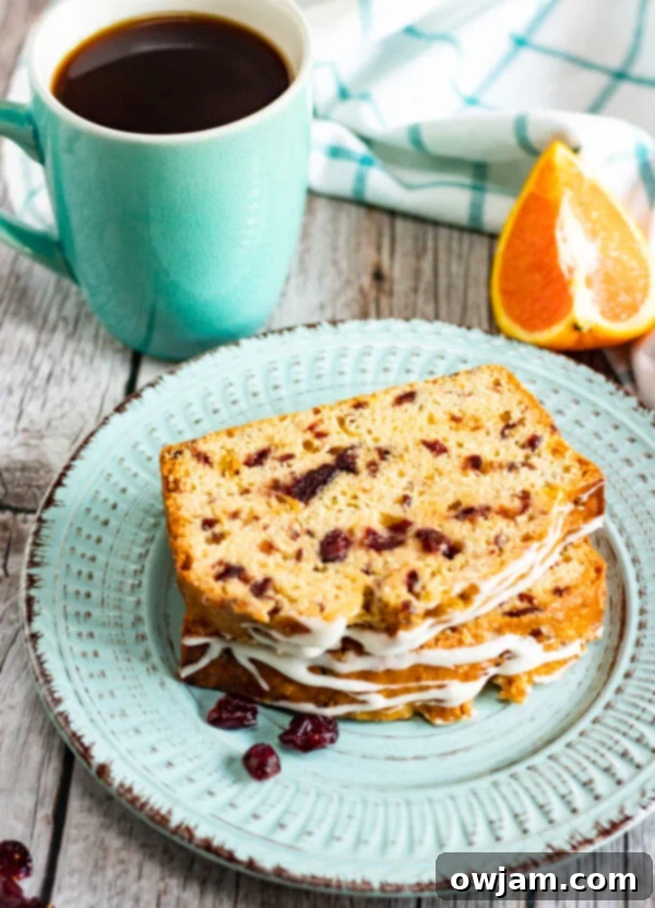 A whole Cranberry Orange Bread loaf and a sliced portion on a white plate