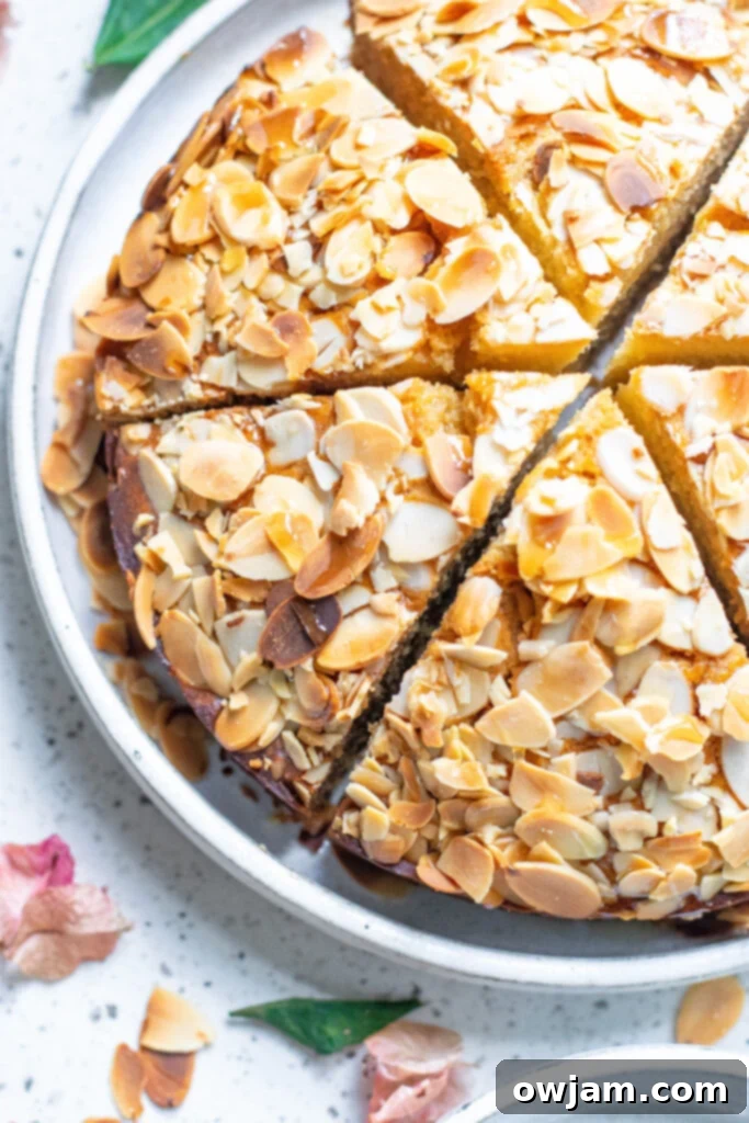 Irresistible Almond Cake 2 A beautiful slice of moist Honey Almond Cake on a white plate, garnished with toasted almonds and a hint of honey drizzle