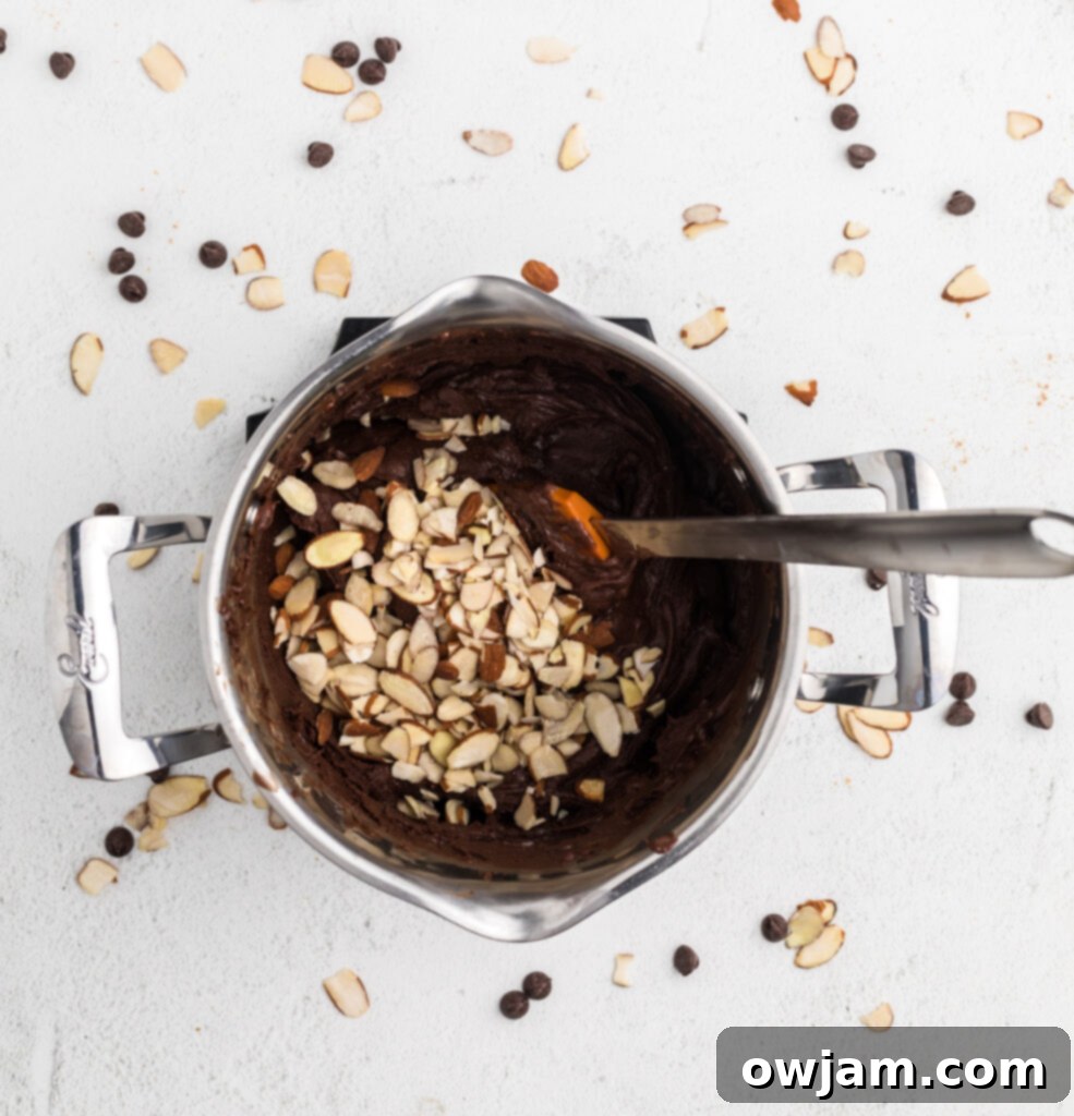 Stirring almond extract and slivered almonds into melted chocolate fudge mixture.