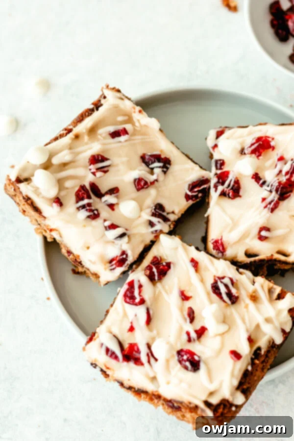 A stack of finished Cranberry Bliss Bars, generously frosted and drizzled with white chocolate, on a decorative plate.