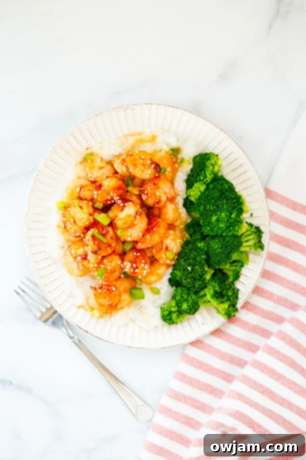 Honey Garlic Sriracha Shrimp served on a pristine white plate, garnished with fresh green onions and sesame seeds.